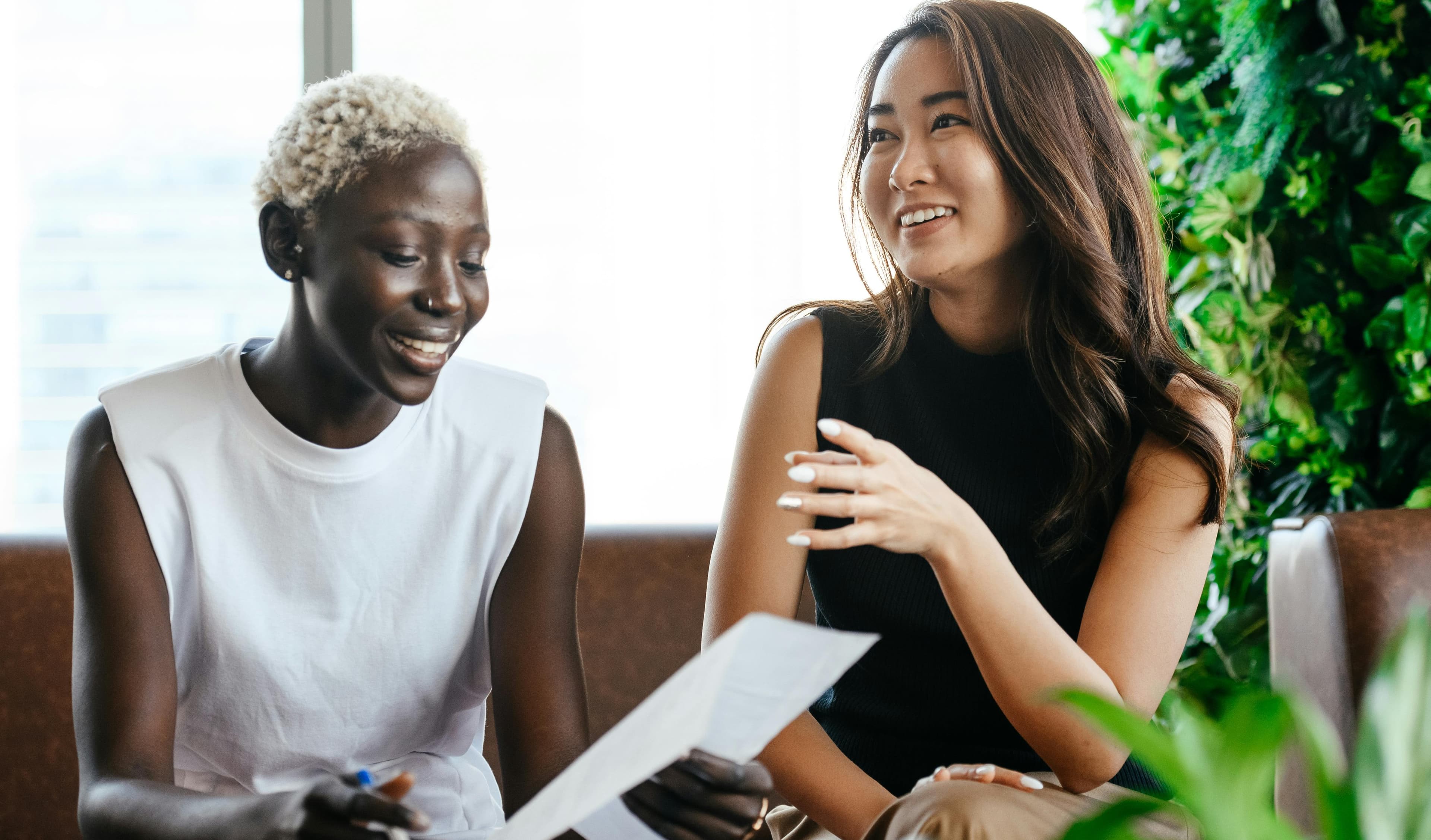 Two women having a conversation in a professional setting with greenery in the background